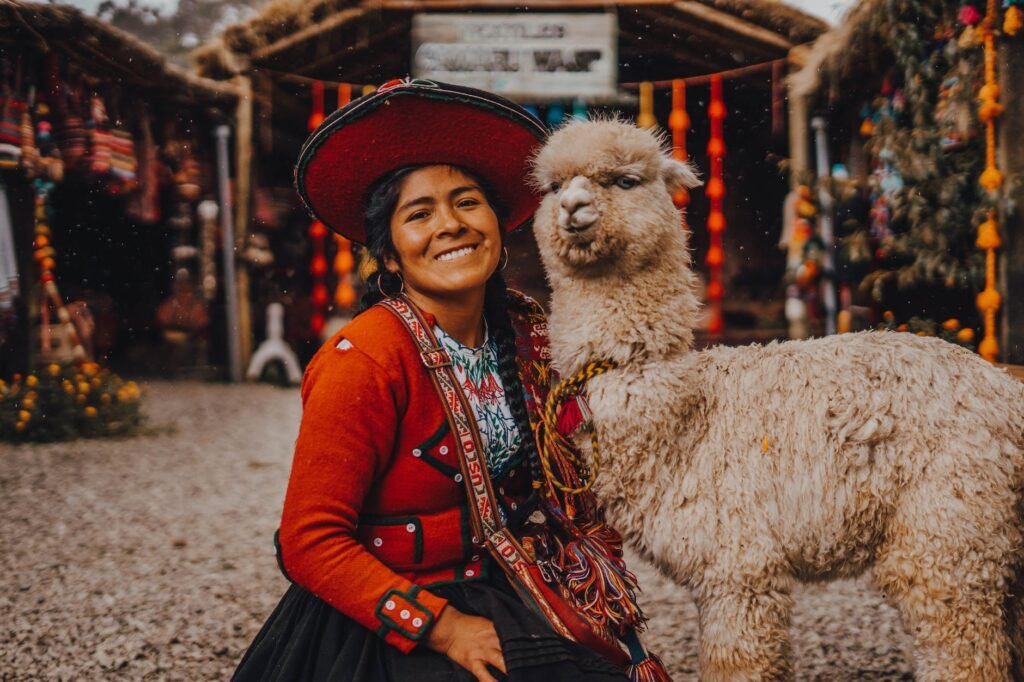young woman in traditional clothing and sitting next to an alpaca